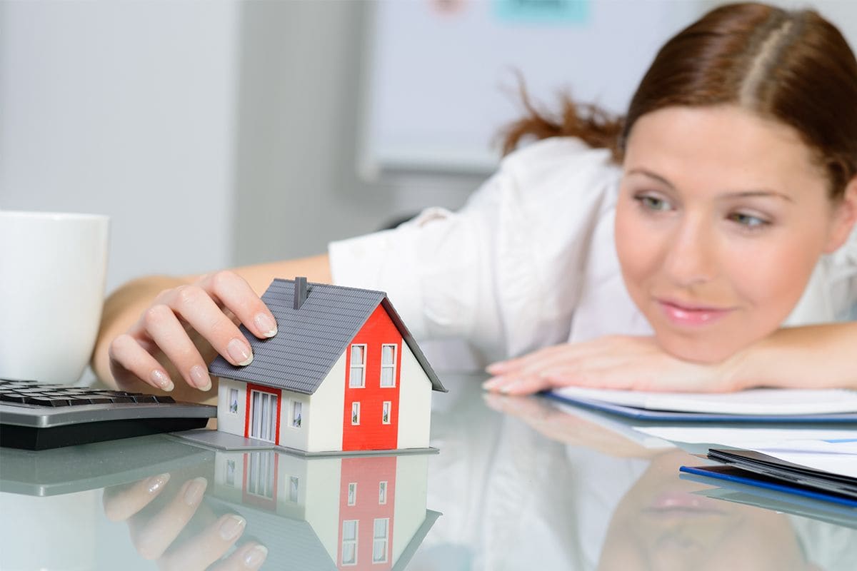 Dreamy young woman behind desk playing with toy house