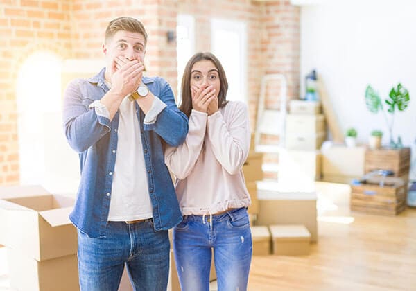Young couple moving to a new house shocked covering mouth with hands for mistake