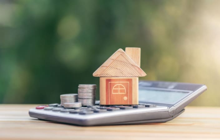 Miniature house and coins over pocket calculator