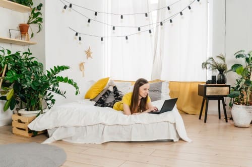 Smiling woman using laptop at home in bedroom.