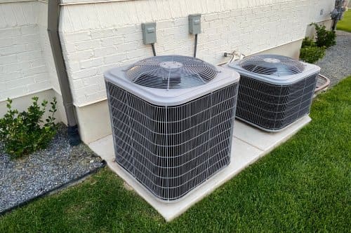 Double AC units outside white brick home with green landscape and gravel