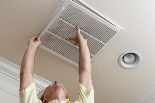 Senior male reaching up to open filter holder for air conditioning filter in ceiling