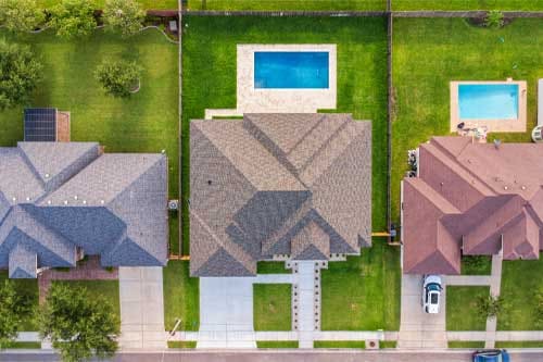 Three houses with a swimming pool in the backyard, surrounded by greenery and outdoor seating areas.