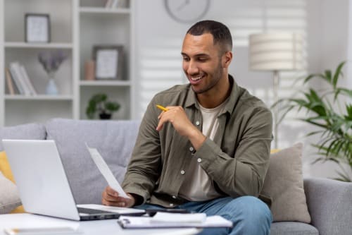 Man at home sitting on sofa in living room, calculating and paying bills, man with calculator and laptop online paying for rent and loan.