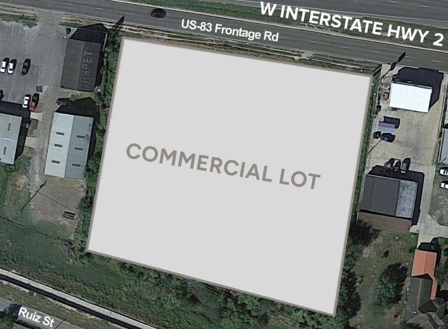 Aerial view of a vacant commercial lot labeled "COMMERCIAL LOT," bordered by roads and nearby buildings.