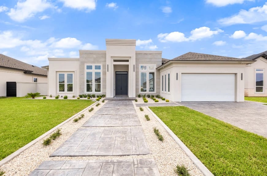 Modern single-story home with a landscaped front yard, stone pathway, and a two-car garage under a blue sky.